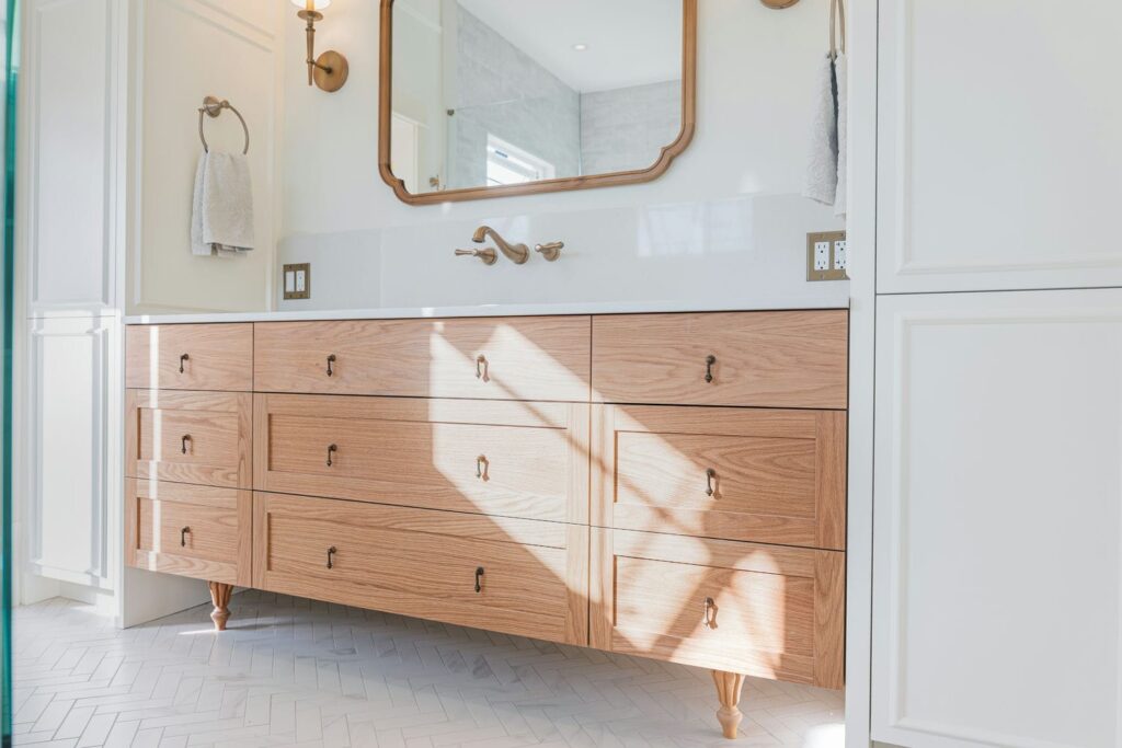 White oak bathroom vanity on turned wooden feet with brass drop pulls and a white quartz top