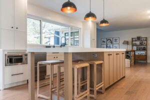 Open plan kitchen with a white oak seating island, oak bar stools and painted perimeter cabinets