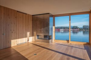 Floor to ceiling white oak wall panelling and a metal clad fireplace in a waterfront living room