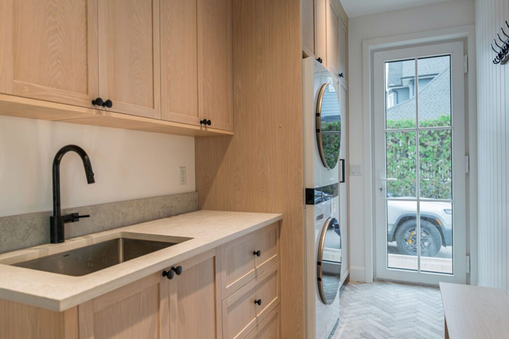 Laundry room built ins in white oak with a stone counter, sink and stacked washer dryer tower