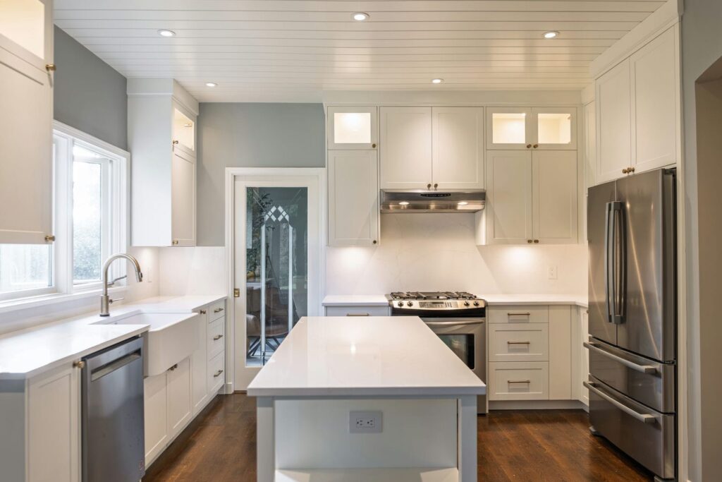 Painted white Shaker kitchen with a quartz island, glass front upper cabinets and apron sink