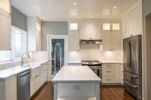 Painted white Shaker kitchen with a quartz island, glass front upper cabinets and apron sink