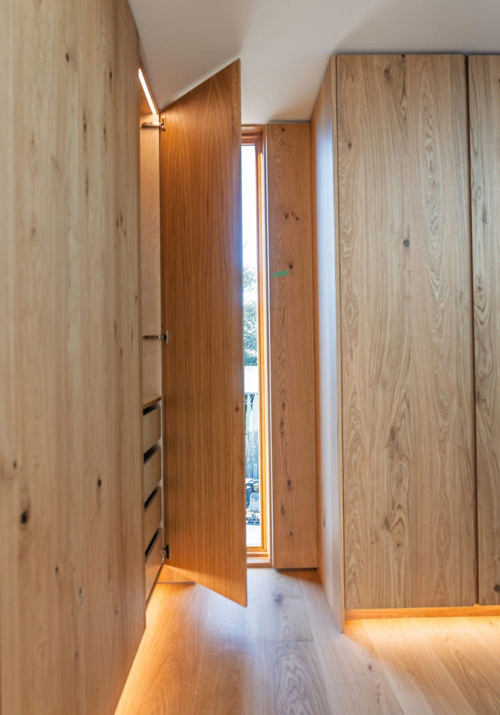 Walk in closet with an oak cabinet door open on interior drawers and lit toe kick along the floor